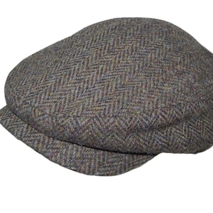 Pode incluir: Boné plano de tweed castanho com padrão de espinha de peixe. O boné tem uma coroa arredondada e uma aba pequena e rígida. O tecido é uma mistura de fios castanhos, azuis e verdes.