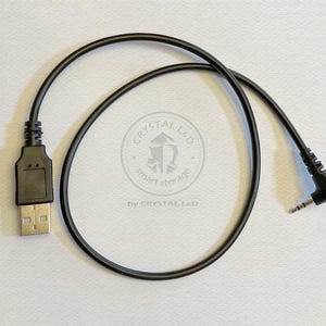 May include: A black USB to 3.5mm audio cable. The USB connector is rectangular, and the 3.5mm connector is angled. The cable is coiled and lies on a white surface. The text "CRYSTAL L&D smart storage" is visible.