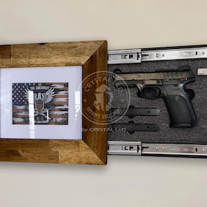 Pode incluir: Uma moldura de madeira com uma impressão de uma bandeira americana e o texto "The 2nd Amendment" dentro. A moldura está aberta para revelar um cofre de armas preto com uma pistola dentro.