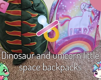 May include: Two children's backpacks. One is green with a dinosaur design and red accents. The other is pink with a unicorn, rainbow, and star design. Text on the image reads "Dinosaur and unicorn little space backpacks."