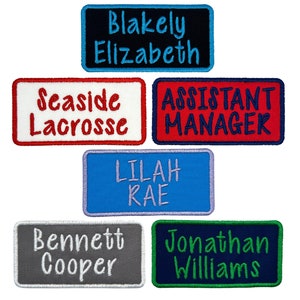 May include: Six embroidered patches with various text. The top patch is black with blue text that reads "Blakely Elizabeth". The patch below it is red with white text that reads "Seaside Lacrosse". The patch to the right of the top patch is red with blue text that reads "Assistant Manager". The patch below the red patch is blue with purple text that reads "Lilah Rae". The patch to the left of the blue patch is gray with white text that reads "Bennett Cooper". The patch to the right of the blue patch is dark blue with green text that reads "Jonathan Williams".