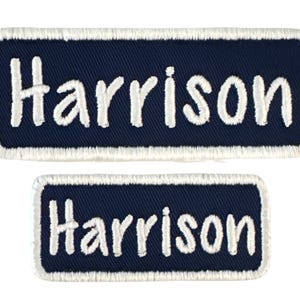 May include: Two white embroidered patches with a navy blue background. The patches are rectangular and have the name "Harrison" written in white on them.
