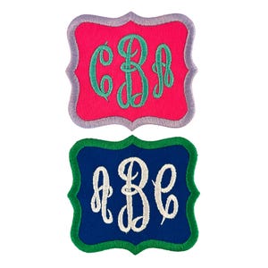 May include: Two embroidered fabric patches with monogram initials. The top patch is pink with a teal green monogram "C B A". The bottom patch is navy blue with a white monogram "A B C".