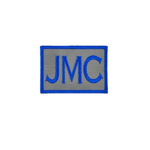 May include: A gray rectangular patch with a blue border and the letters "JMC" embroidered in blue.