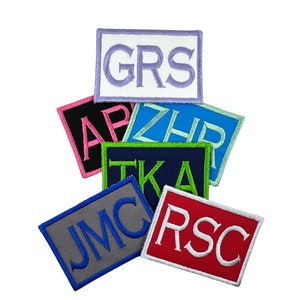 May include: A stack of colorful embroidered patches with different letters and initials. The patches are made of felt and have a white border. The letters are in a variety of colors, including pink, blue, green, and white.