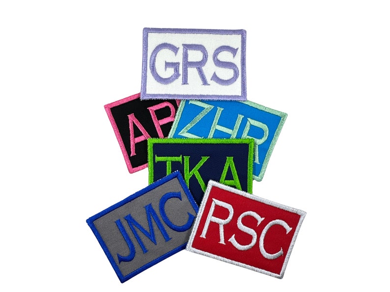 May include: A stack of colorful embroidered patches with different letters and initials. The patches are made of felt and have a white border. The letters are in a variety of colors, including pink, blue, green, and white.