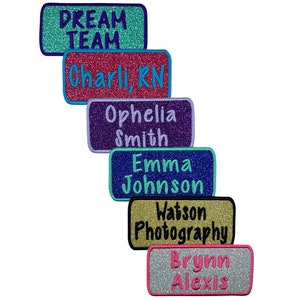 May include: Six glitter iron-on patches with various names and phrases. The patches are in different colors, including teal, pink, purple, blue, gold, and silver. The text on the patches includes "Dream Team", "Charli RN", "Ophelia Smith", "Emma Johnson", "Watson Photography", and "Brynn Alexis".