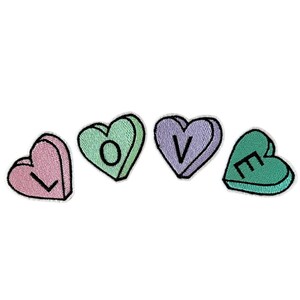 May include: Four embroidered iron-on patches shaped like candy hearts, each with a letter of the word "LOVE" in black. The hearts are in shades of pink, green, and purple.