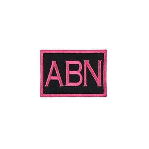 May include: A black rectangular patch with pink stitching. The letters "ABN" are embroidered in pink on the patch.