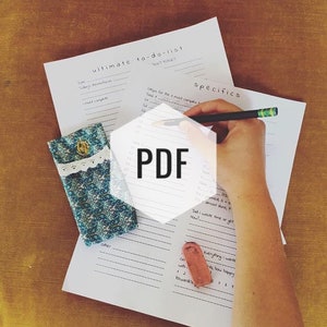 May include: A white to-do list with the words "ultimate to-do-list" and "specifics" written in black ink. The list is divided into two columns, one for tasks and one for specifics. A hand is writing on the list with a black pen. A small blue and white patterned pouch is in the lower left corner of the image.