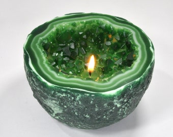 May include: A green candle shaped like a geode with a white interior and a lit wick in the center.