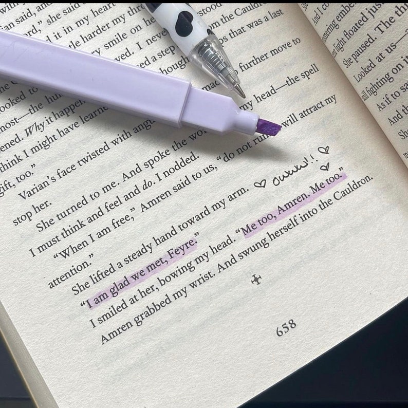 May include: Open book with highlighted text and a purple highlighter. A black and white pen with heart accents rests on the page. The highlighted text reads, "I am glad we met, Feyre."