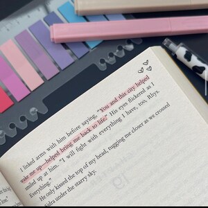 May include: Open book with highlighted text and a cow-print pen. The text reads, "You and this city helped bring me back to life." Colorful sticky notes and pens are in the background, suggesting a study or reading theme.