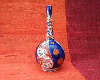 May include: A blue and white ceramic vase with a long neck and a round body. The vase is decorated with floral and geometric patterns in red, blue, and white.