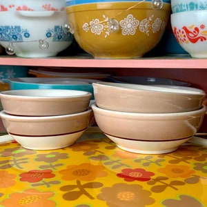 May include: A set of four brown and white ceramic bowls stacked on top of each other. The bowls are sitting on a yellow table cloth with a floral pattern.