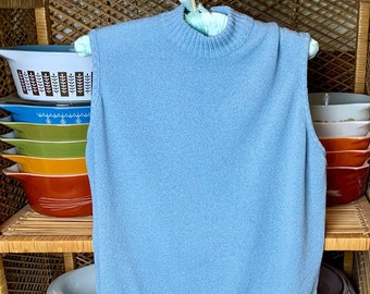 May include: A light blue knitted sleeveless sweater hanging on a wooden shelf with a variety of colorful bowls stacked on the shelves above and below.