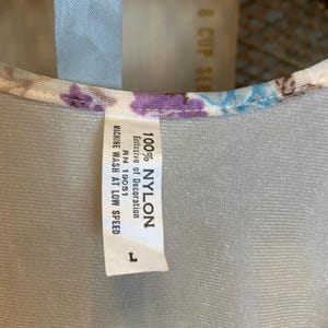 May include: A white nylon fabric with a floral print and a white tag that reads "100% NYLON", "Exclusive of Decoration", "RN 19051", "MACHINE WASH AT LOW SPEED", and "L".