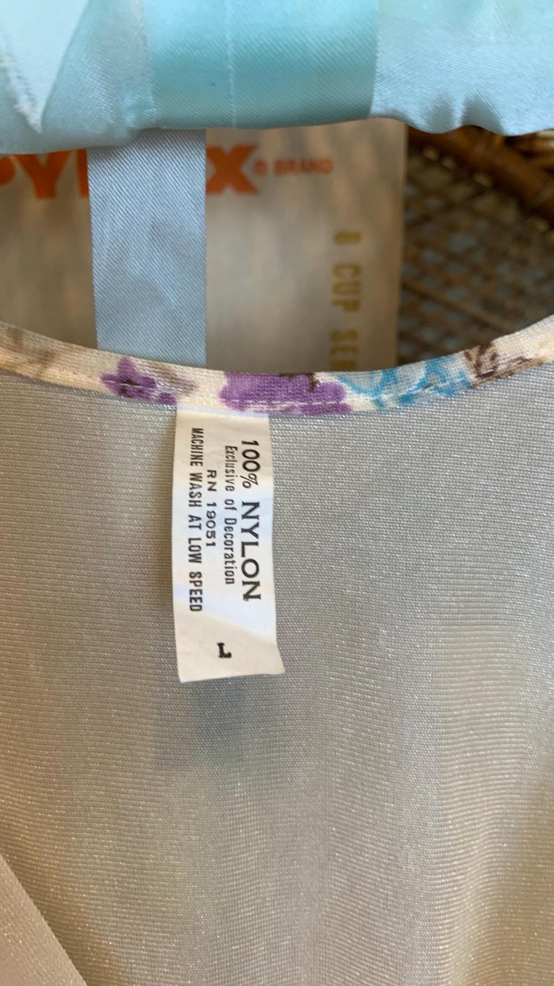 May include: A white nylon fabric with a floral print and a white tag that reads "100% NYLON", "Exclusive of Decoration", "RN 19051", "MACHINE WASH AT LOW SPEED", and "L".