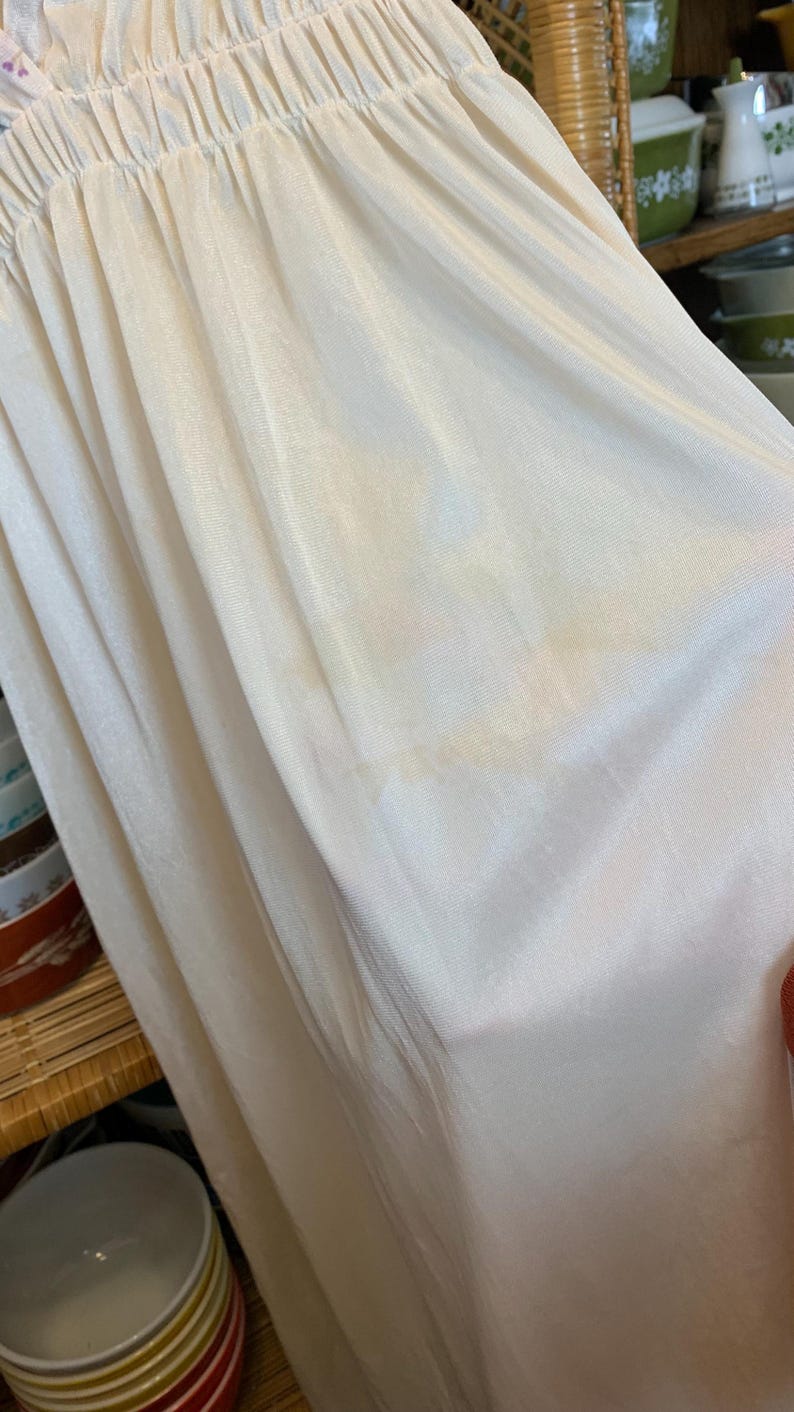 May include: A white slip with a gathered elastic waistband. The slip is made of a soft, silky fabric.