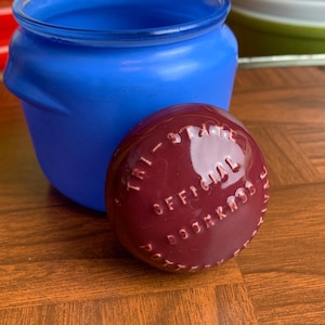 May include: A blue glass jar with a maroon lid. The lid has the words "Tri-State Official Door Knobs" written on it.