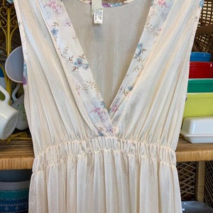 May include: A white sleeveless nightgown with a floral print and a V-neckline. The neckline is trimmed with a floral lace. The nightgown is made of a sheer fabric.