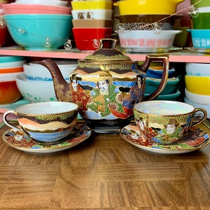 May include: A Japanese tea set with a teapot and two cups. The teapot and cups are decorated with colorful floral and geometric patterns. The teapot has a gold handle and spout. The cups have gold rims.