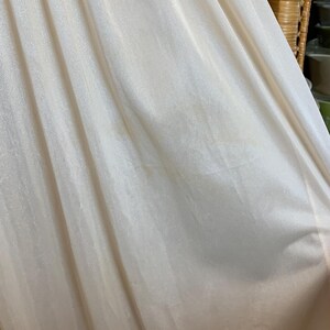 May include: Close-up of a white, sheer fabric with a smooth, silky texture. The fabric is gathered at the top and has a slight sheen.