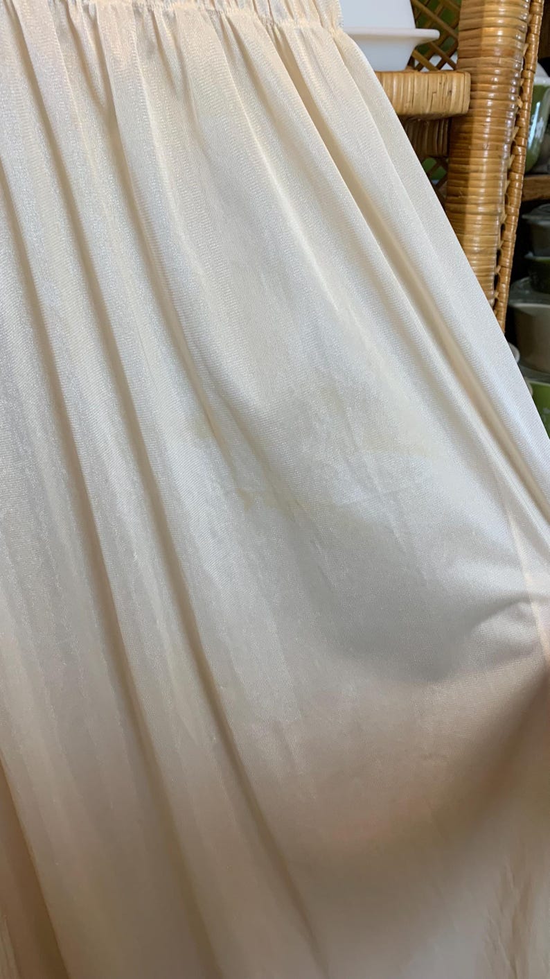 May include: Close-up of a white, sheer fabric with a smooth, silky texture. The fabric is gathered at the top and has a slight sheen.