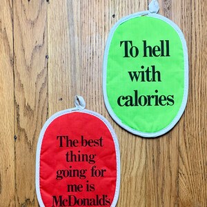 May include: Two red and green oven mitts with white trim. The red mitt says "The best thing going for me is McDonald's". The green mitt says "To hell with calories".