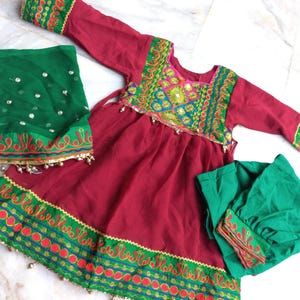 May include: A maroon dress with green and red embroidery, a green dupatta, and a green churidar. The dress has a gathered skirt and a round neckline. The dupatta is sheer and has a silver sequin design. The churidar is solid green.