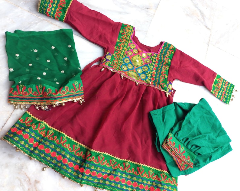 May include: A maroon dress with green and red embroidery, a green dupatta, and a green churidar. The dress has a gathered skirt and a round neckline. The dupatta is sheer and has a silver sequin design. The churidar is solid green.