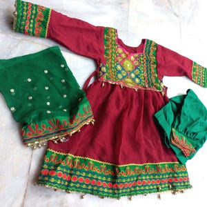 May include: A red dress with green and gold embroidery, a green dupatta with gold sequins, and a green cap. The dress has a gathered skirt and a fitted bodice.