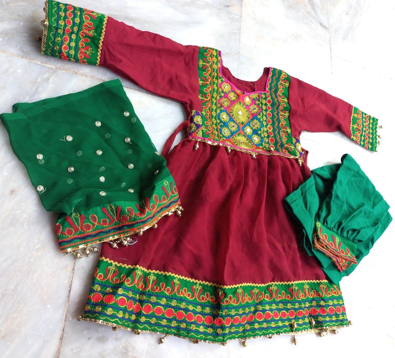 May include: A red dress with green and gold embroidery, a green dupatta with gold sequins, and a green cap. The dress has a gathered skirt and a fitted bodice.