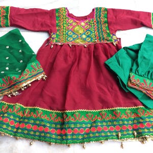 May include: A red dress with green and gold embroidery, a green dupatta with gold embroidery, and a green salwar with gold embroidery. The dress has a round neckline and long sleeves. The dupatta is a long scarf that is worn over the head and shoulders. The salwar is a pair of loose-fitting pants.