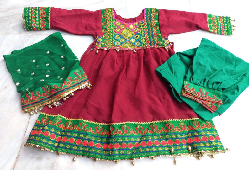 May include: A red dress with green and gold embroidery, a green dupatta with gold embroidery, and a green salwar with gold embroidery. The dress has a round neckline and long sleeves. The dupatta is a long scarf that is worn over the head and shoulders. The salwar is a pair of loose-fitting pants.