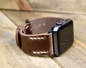 May include: A brown leather watch band with white stitching for an Apple Watch.