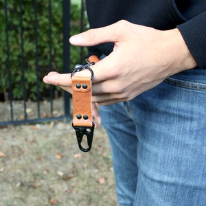 May include: A brown leather key chain with a black metal clip and two black rivets.