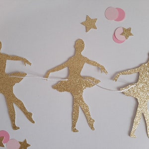 May include: A gold glitter ballerina garland with pink and gold stars. The garland is strung with white thread.