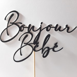 Peut inclure: Un topper de g&acirc;teau noir paillet&eacute; avec le texte "Bonjour B&eacute;b&eacute;" sur un b&acirc;tonnet en bois.