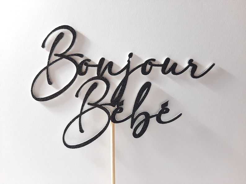 Peut inclure: Un topper de g&acirc;teau noir paillet&eacute; avec le texte "Bonjour B&eacute;b&eacute;" sur un b&acirc;tonnet en bois.