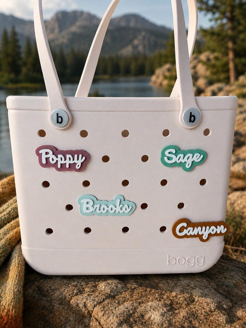 Puede incluir: Un bolso tote perforado de color rosa claro con dos asas y la palabra bogg grabada en la parte inferior. Cuatro inserciones de nombres personalizadas est&aacute;n fijadas en los agujeros, con los nombres Poppy en granate, Sage en verde azulado, Brooks en azul claro y Canyon en marr&oacute;n.