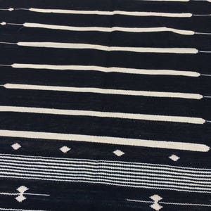 May include: Black and white striped rug with a geometric pattern. The rug has a simple design with horizontal stripes and small diamond shapes.