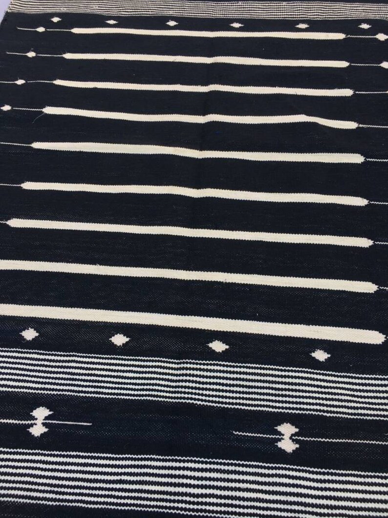 May include: Black and white striped rug with a geometric pattern. The rug has a simple design with horizontal stripes and small diamond shapes.