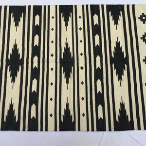 May include: Black and white geometric patterned rug with fringe. The rug has a traditional design with black and white stripes and geometric shapes.
