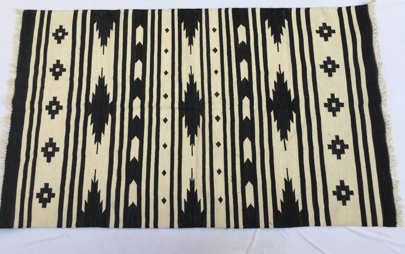 May include: Black and white geometric patterned rug with fringe. The rug has a traditional design with black and white stripes and geometric shapes.