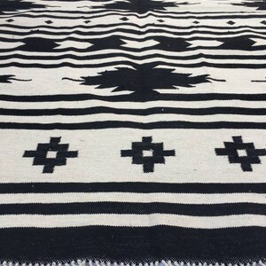 May include: Black and white woven rug with a geometric pattern. The rug has a fringe border.