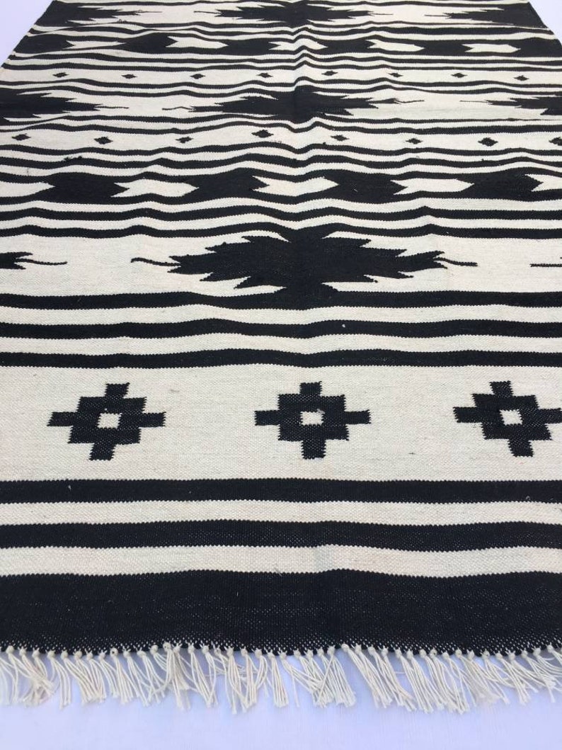 May include: Black and white woven rug with a geometric pattern. The rug has a fringe border.