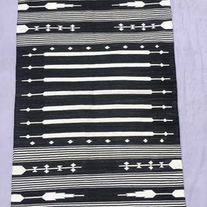 May include: Black and white rug with a geometric pattern. The rug has a fringe border.