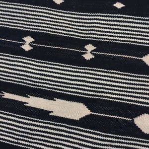 May include: Black and white striped fabric with a geometric pattern. The pattern is made up of thin white lines and thicker white lines that create a diamond shape.