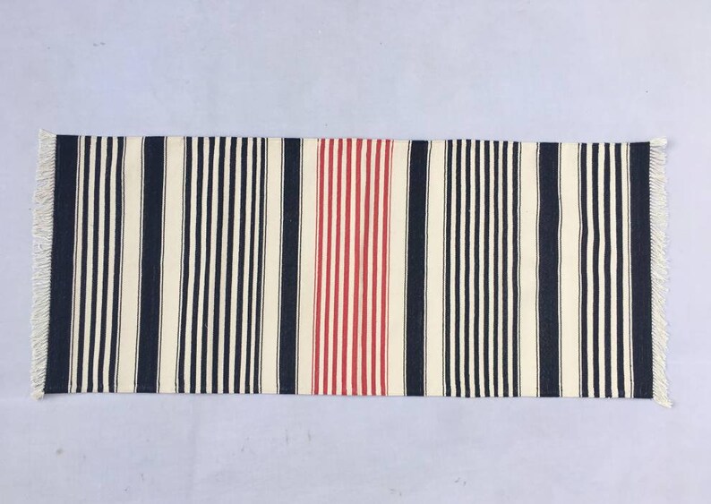 May include: A striped runner rug with black, white and red stripes. The rug has a fringe on both ends.